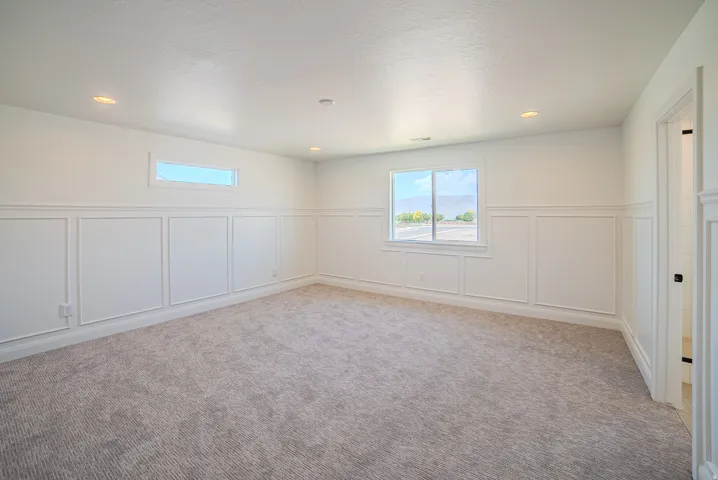 Spacious room featuring wainscoting paneling, recessed lighting, and soft gray carpeting