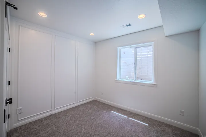 Bright interior space featuring recessed lighting, a window with exterior grating, and textured carpeting