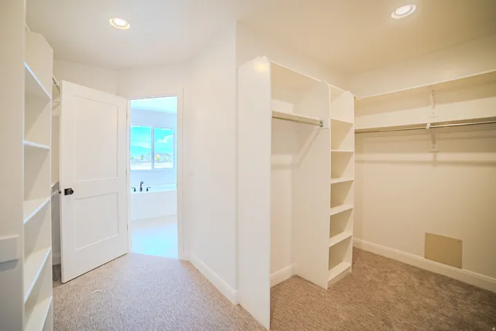 Walk-in closet featuring built-in shelving, hanging rods, recessed lighting, and carpet flooring