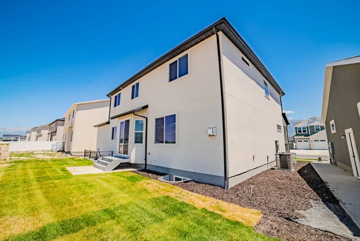 Rear exterior featuring a two-story design, stucco siding, multiple windows, a ground-level patio, and a grass lawn