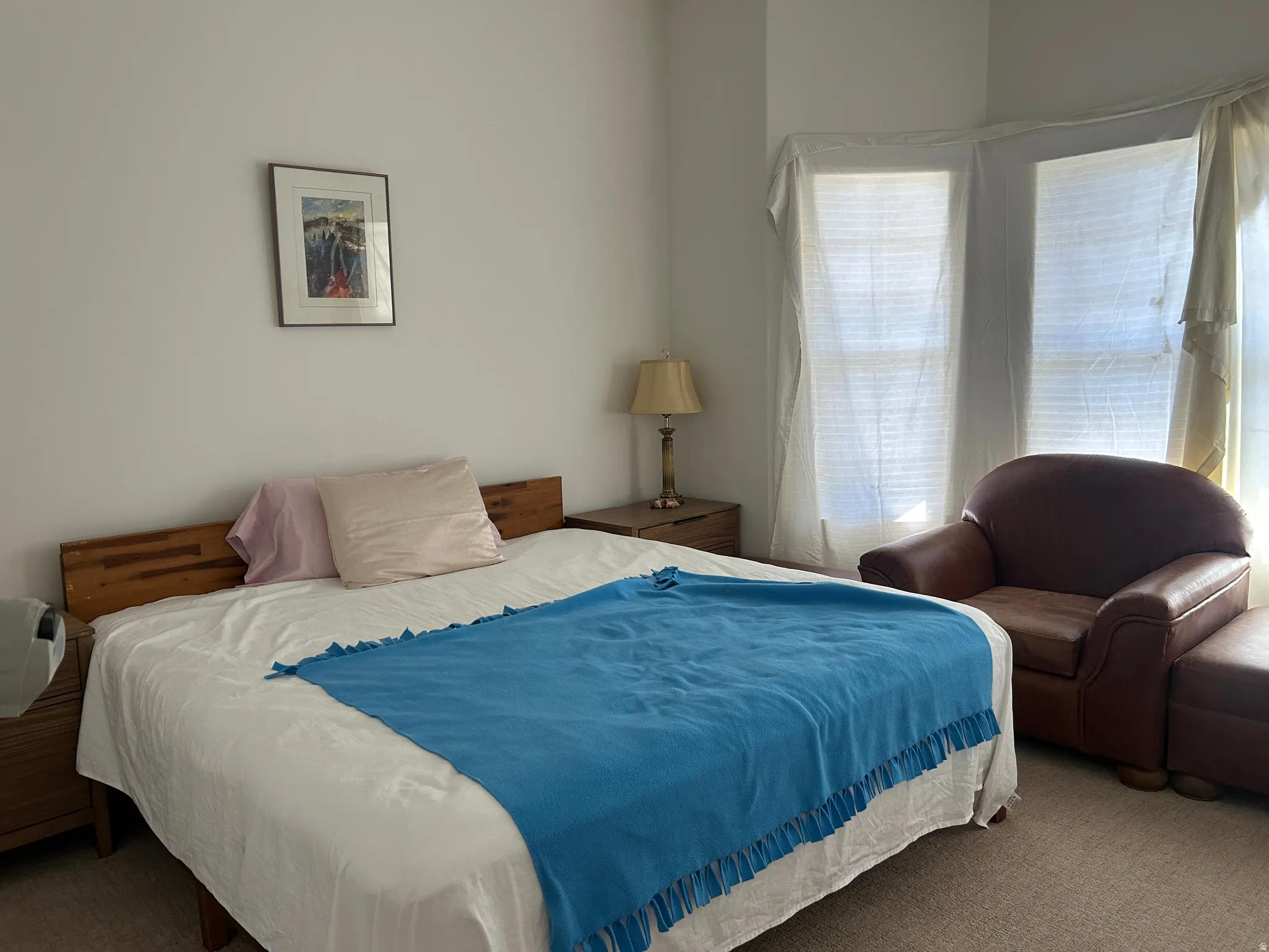 Room featuring a wood-finish headboard and two windows with coverings