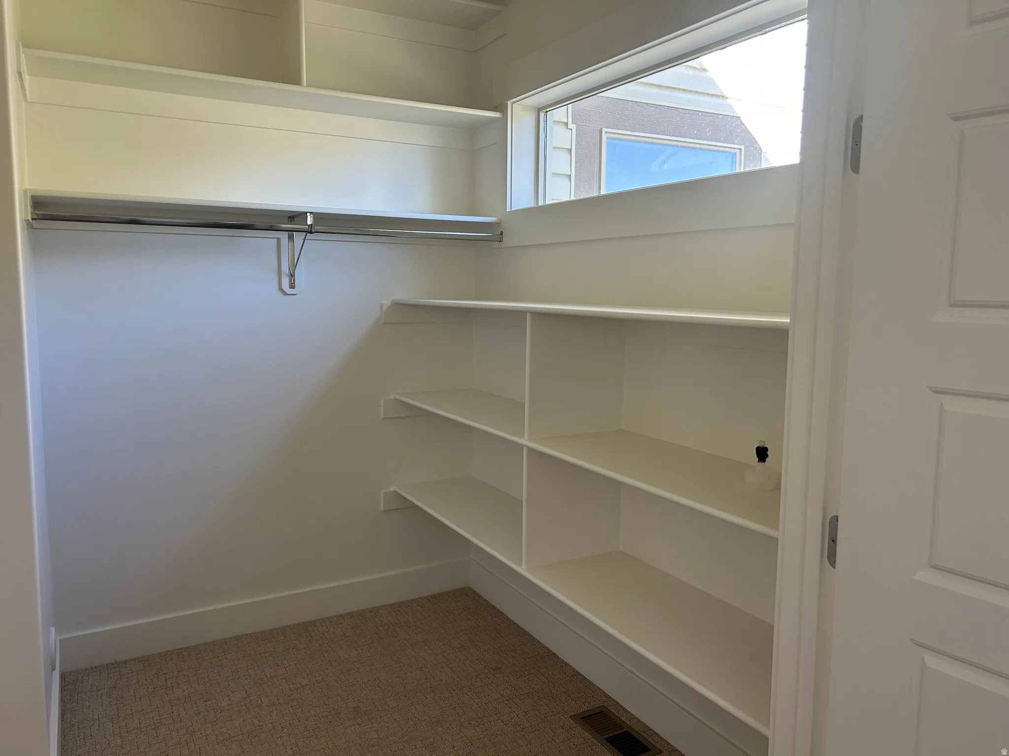 Walk-in closet featuring built-in shelving, a garment rod, and a high horizontal window