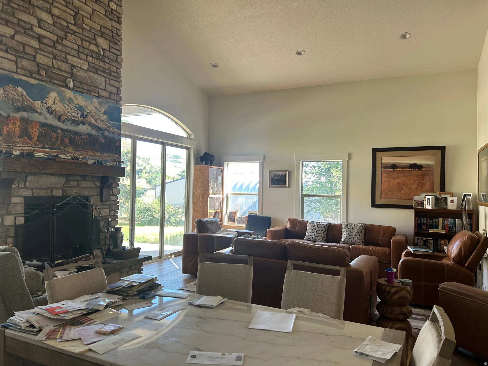 Vaulted ceiling great room featuring a floor-to-ceiling stone fireplace, a substantial wood mantel, recessed lighting, and large sliding glass doors with an arch transom