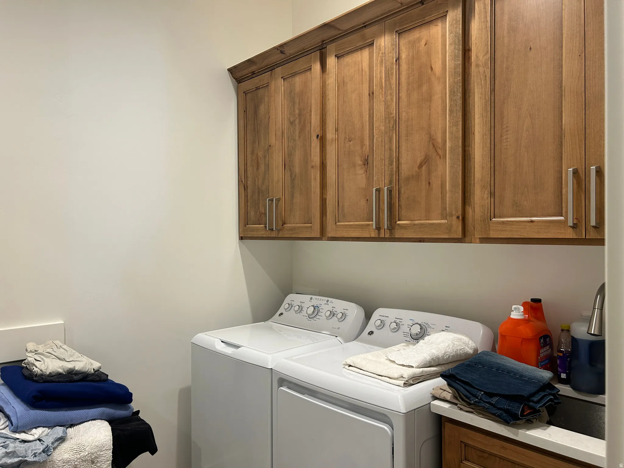 Laundry area featuring built-in wood cabinetry with brushed nickel hardware, a countertop sink, and light-toned walls