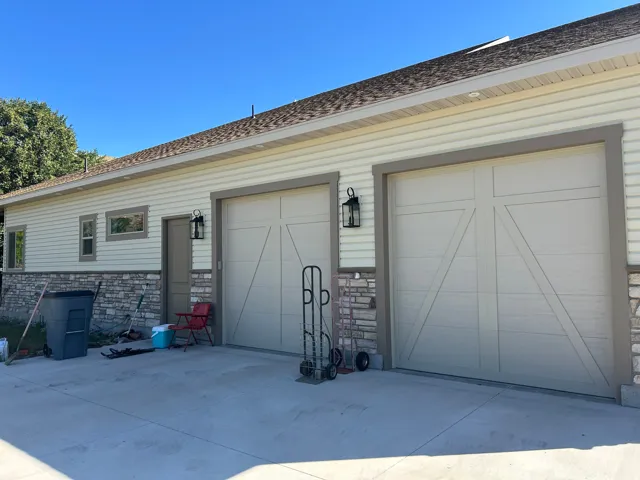Two-car garage featuring carriage-style doors, stone veneer accents, and exterior wall lanterns