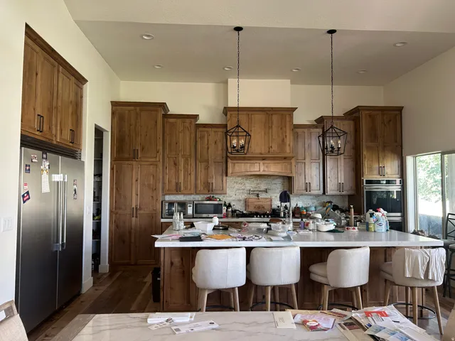 Spacious kitchen featuring extensive wood cabinetry, a large center island with seating, stainless steel appliances, dual wall ovens, and custom pendant lighting fixtures