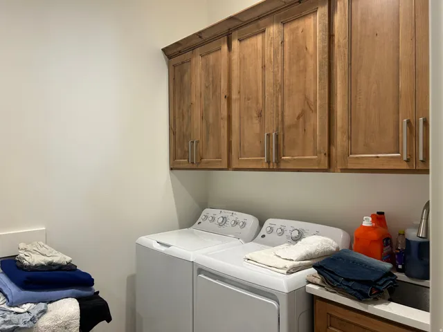 Laundry area featuring built-in wood cabinetry with brushed nickel hardware, a countertop sink, and light-toned walls