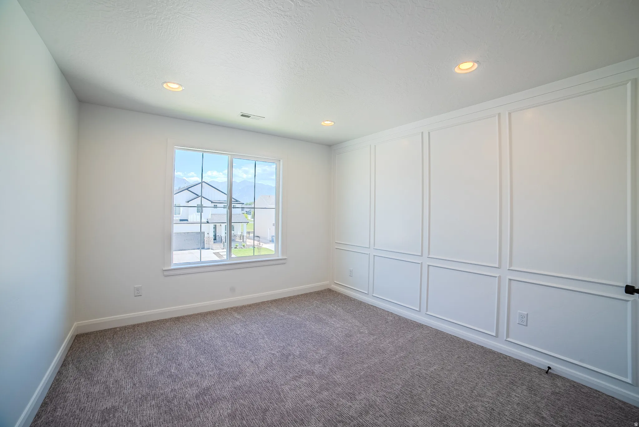 White paneled accent wall complemented by recessed ceiling lighting and grey carpet flooring