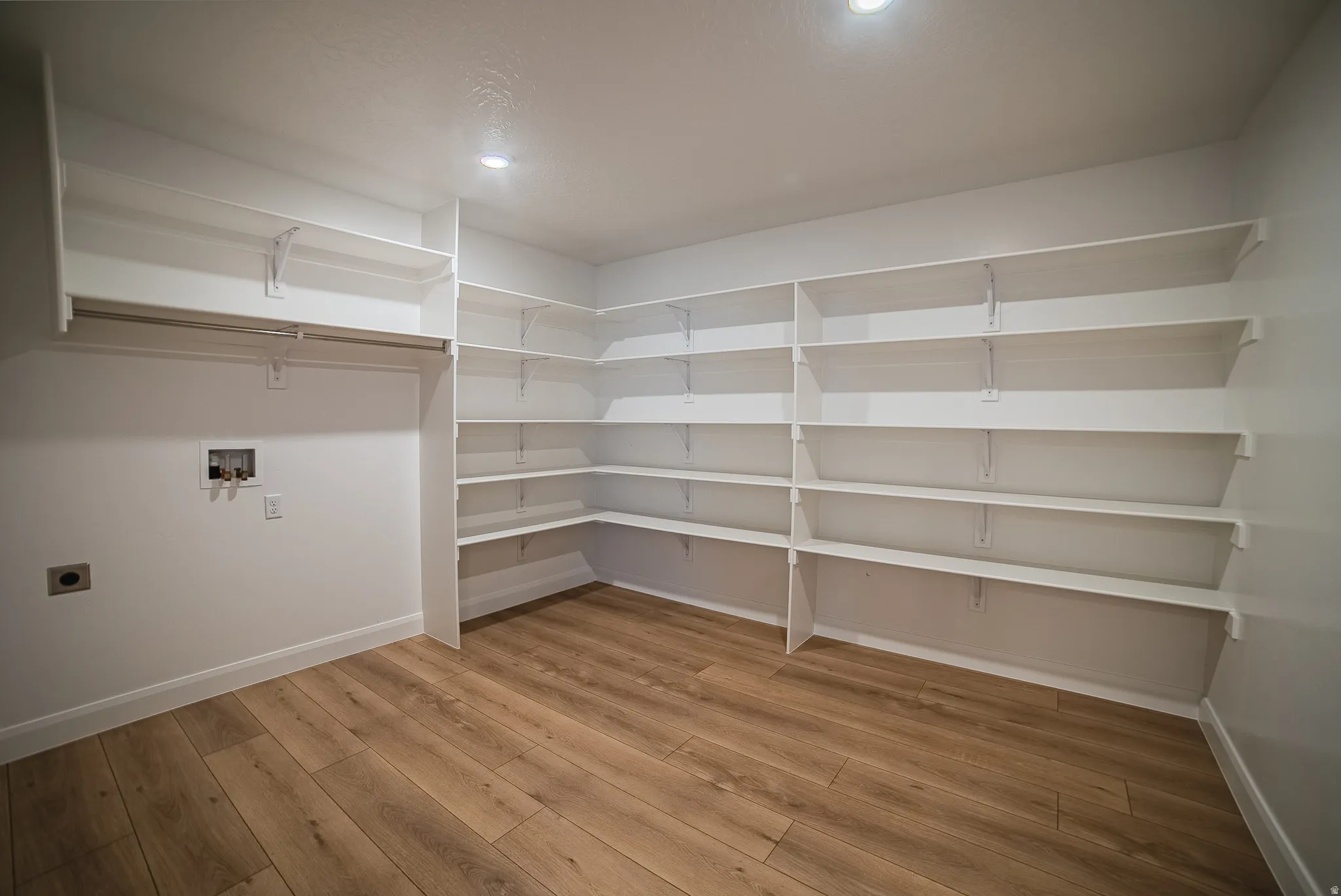Spacious utility room featuring extensive white shelving, a clothing rod, washer/dryer hookups, wood-finish flooring, and recessed lighting