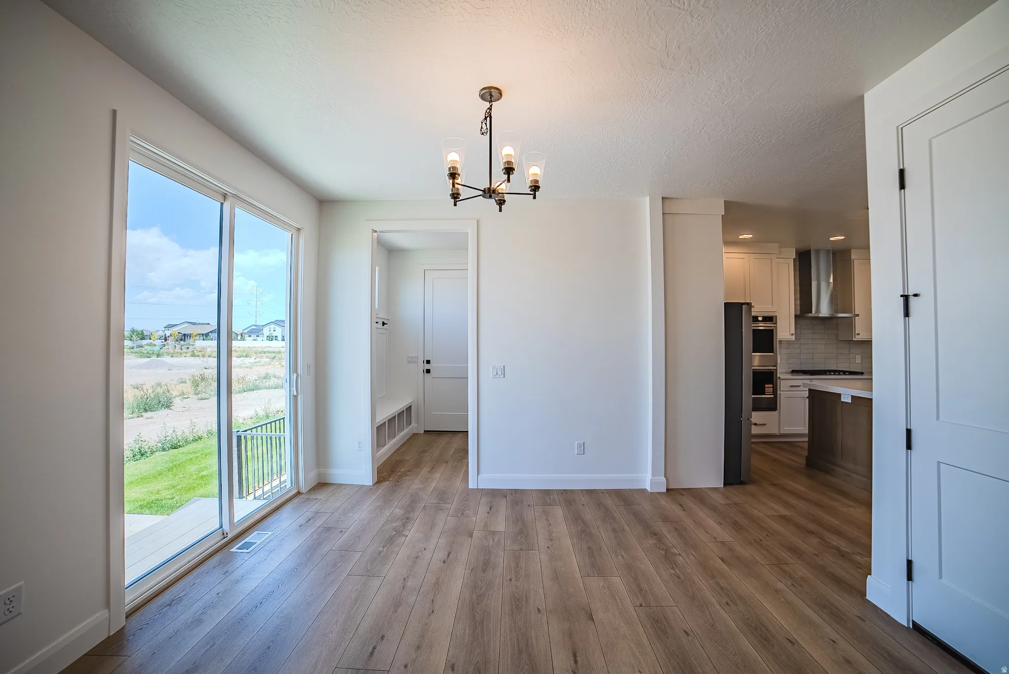 Open-concept dining area featuring wood-finish flooring, a contemporary chandelier, and a sliding glass door to the exterior