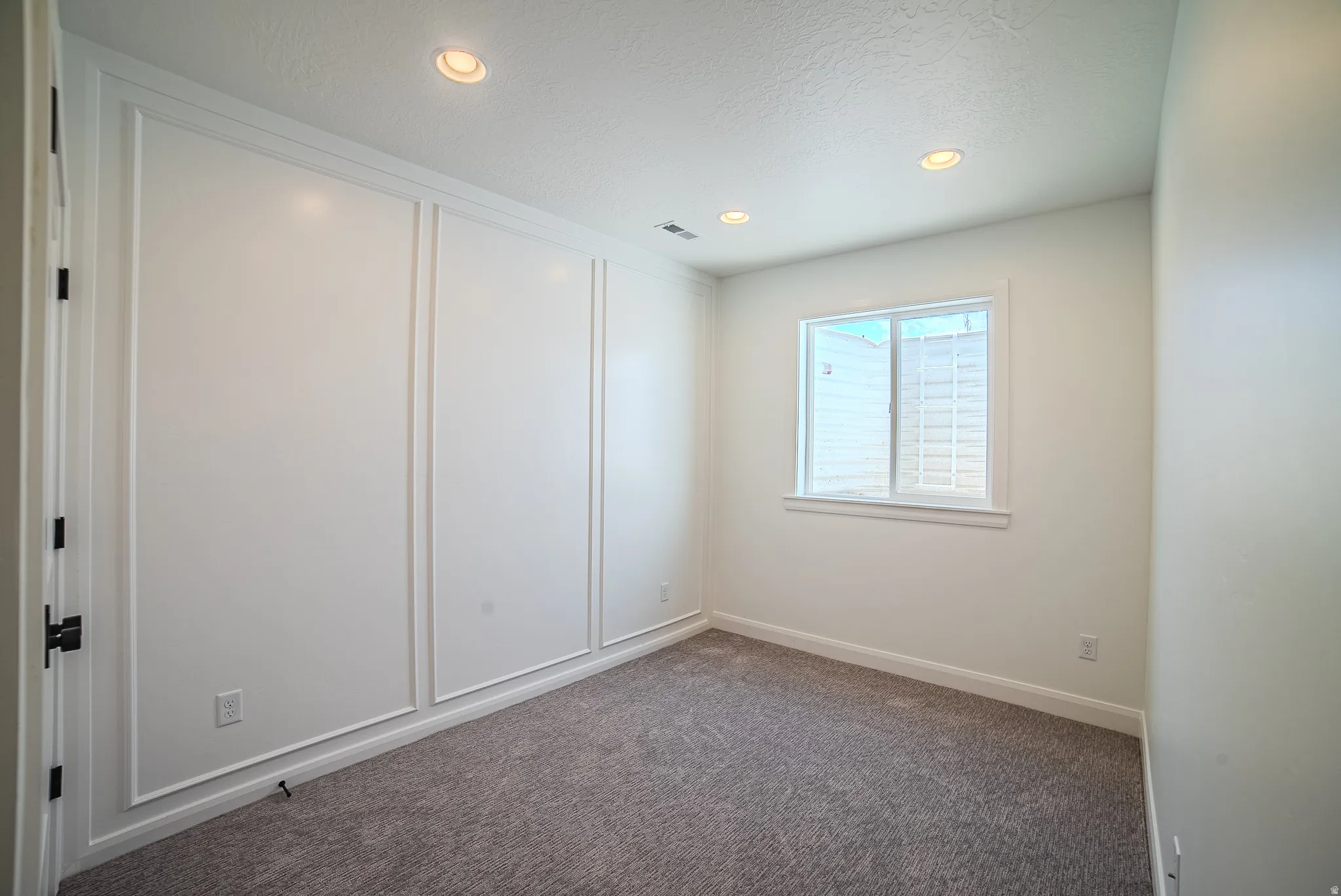 Bright interior space featuring recessed lighting, a window, grey carpet flooring, white baseboards, and wainscoting wall accents
