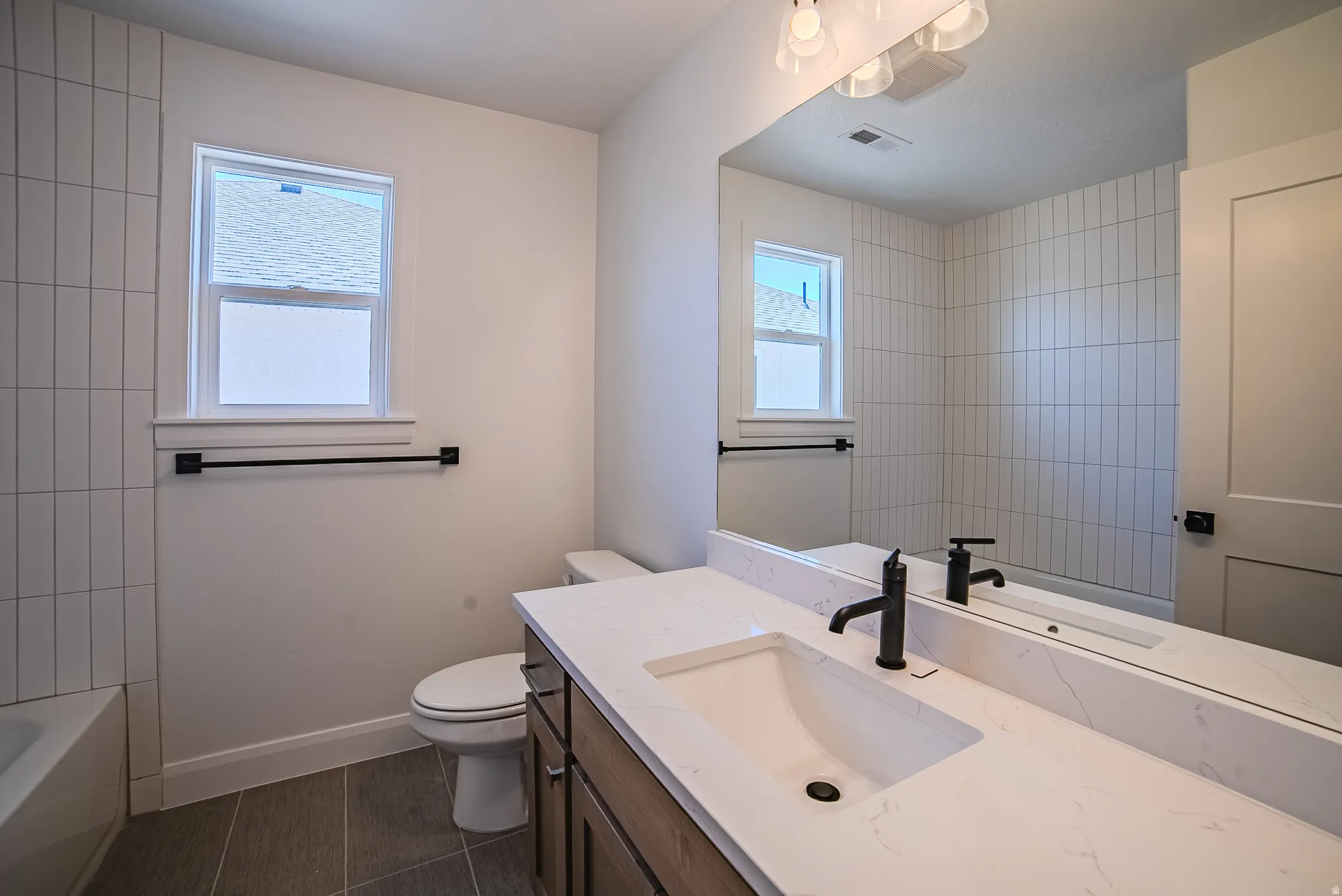 Modern bathroom featuring a wood-finish vanity with a white countertop and integrated sink, matte black faucet, and large wall-mounted mirror