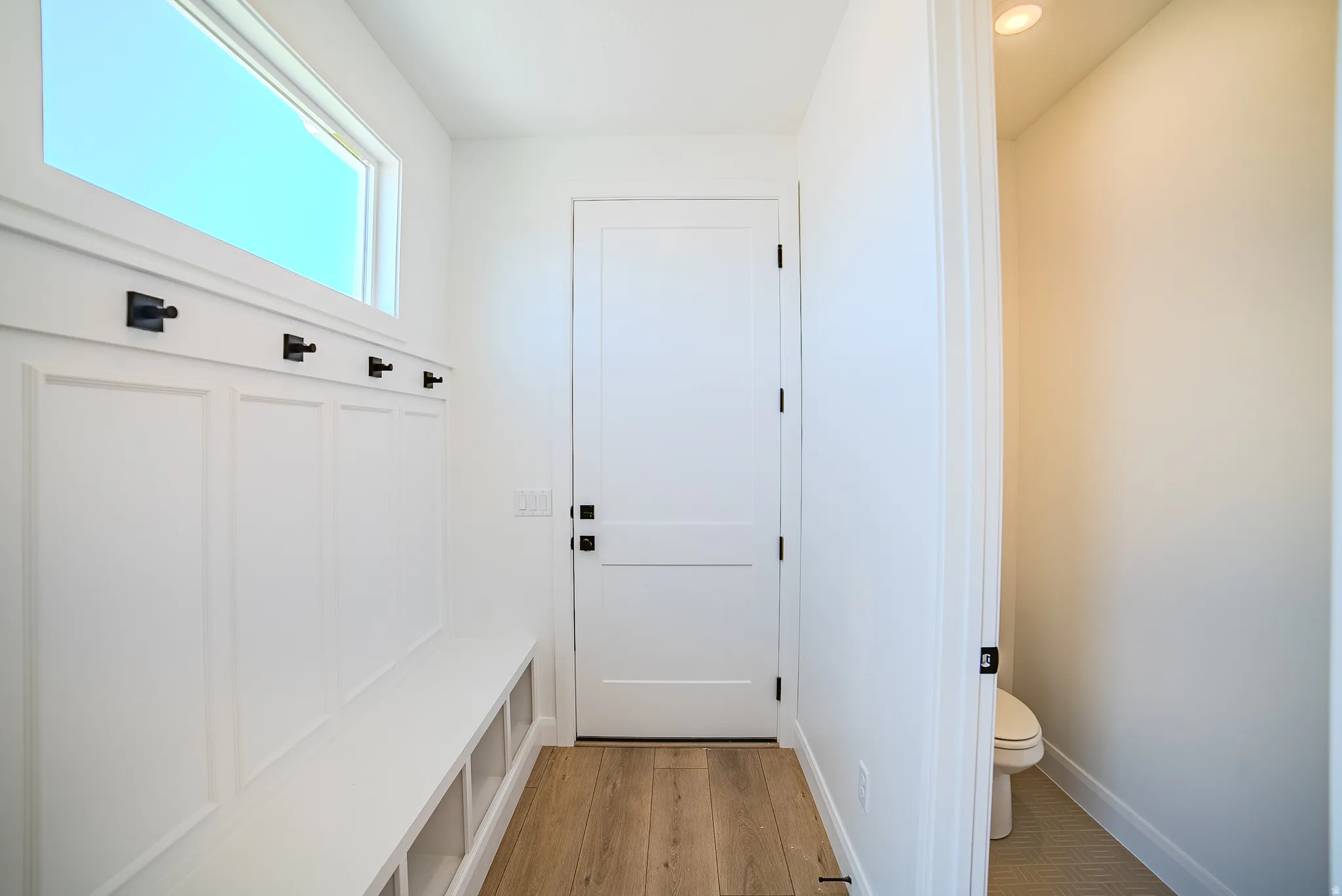Mudroom featuring a built-in bench with storage cubbies, wainscoting, and black wall hooks
