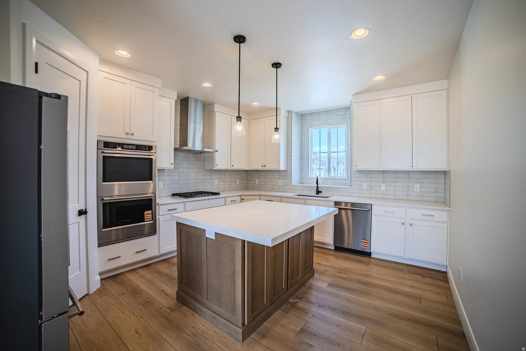 Modern kitchen featuring white shaker cabinets, stainless steel appliances, a center island with a light wood-finish base, light countertops, and wood-finish flooring