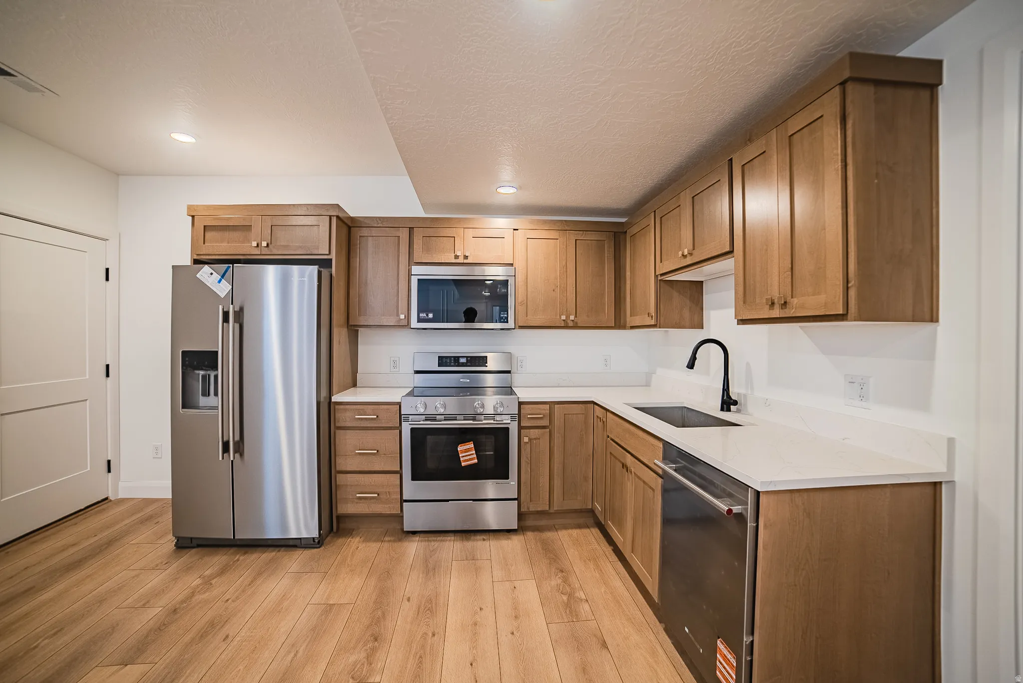 Modern kitchen featuring wood-finish flooring, light wood cabinetry, white countertops, and stainless steel appliances including a refrigerator, range, microwave, and dishwasher