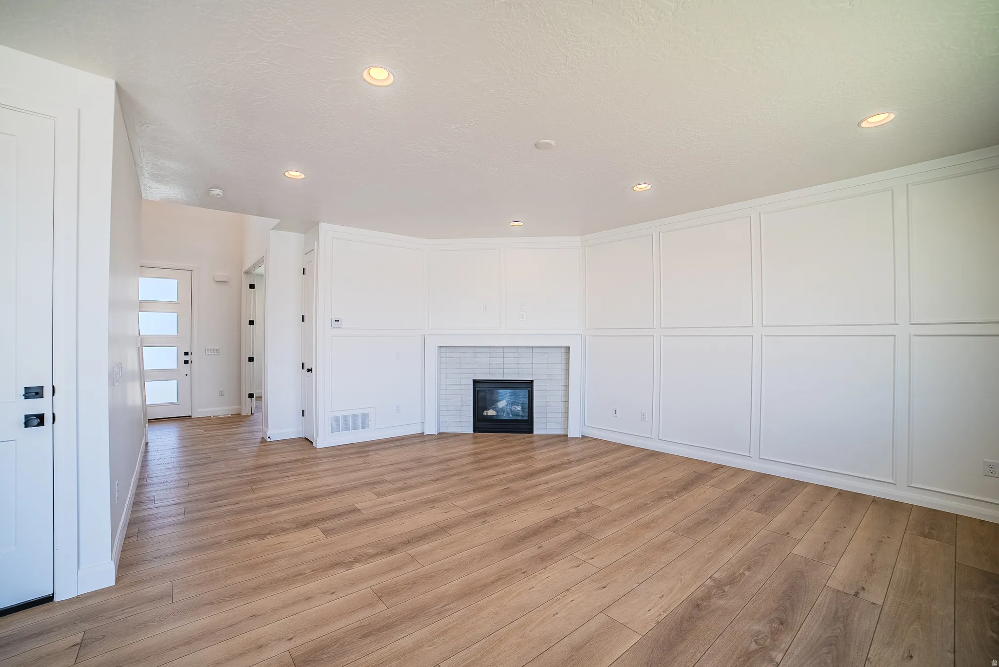 Spacious room featuring wood-finish flooring, recessed lighting, and a contemporary fireplace with white subway tile surround