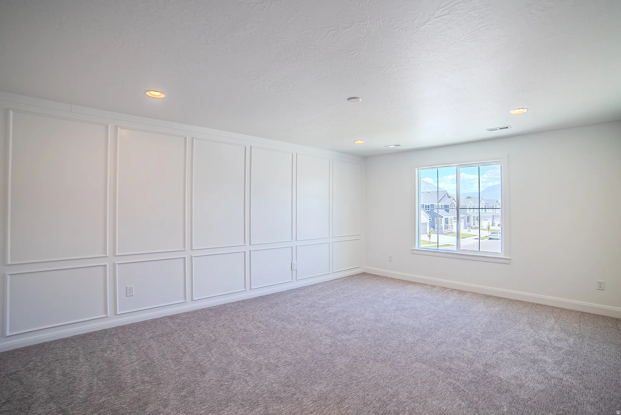Spacious room featuring a decorative accent wall with panel molding, recessed ceiling lighting, and soft carpet flooring