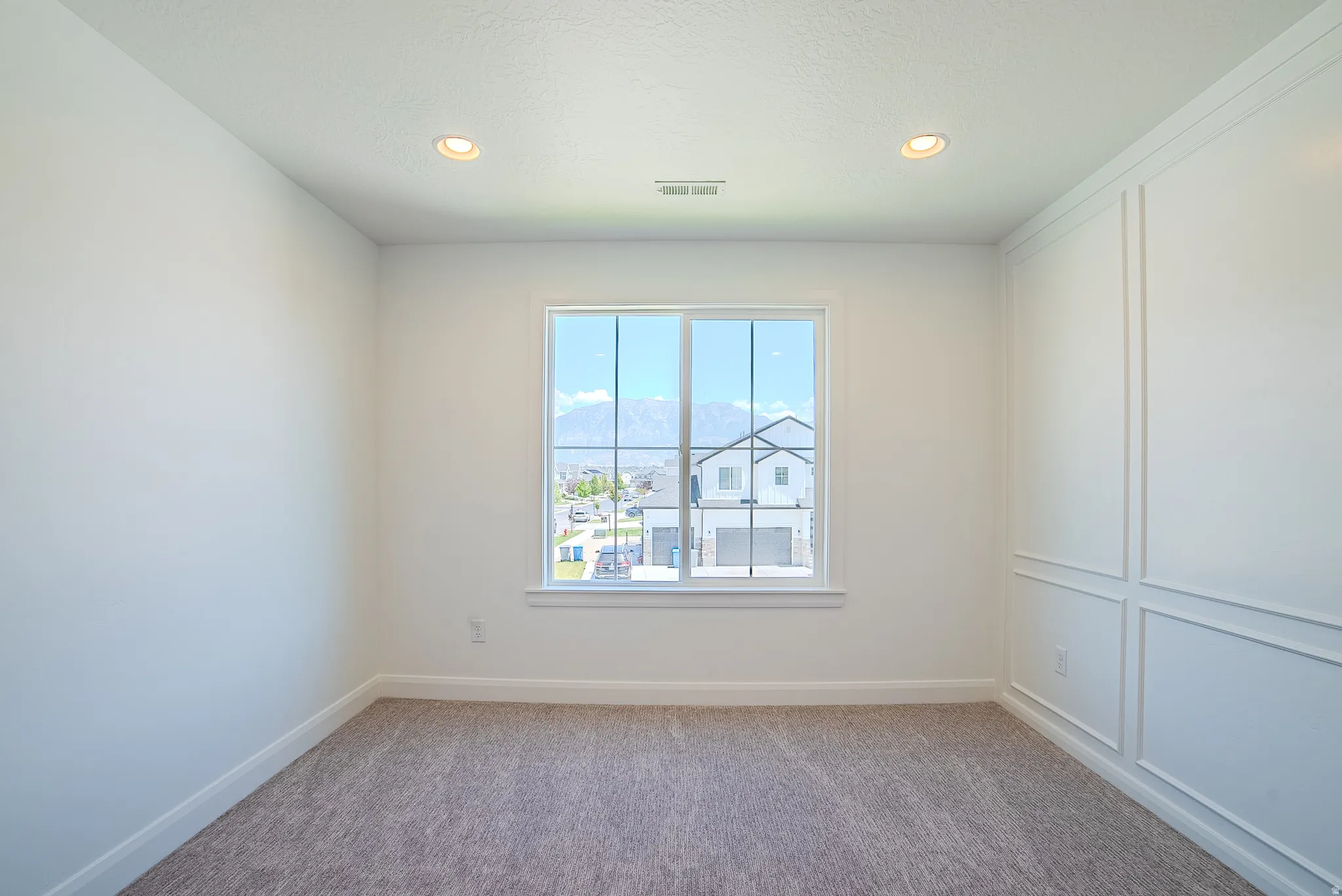 White interior featuring a large window, recessed lighting, wall paneling, and neutral carpeting
