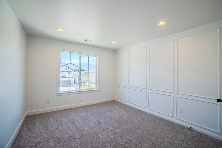 White paneled accent wall complemented by recessed ceiling lighting and grey carpet flooring