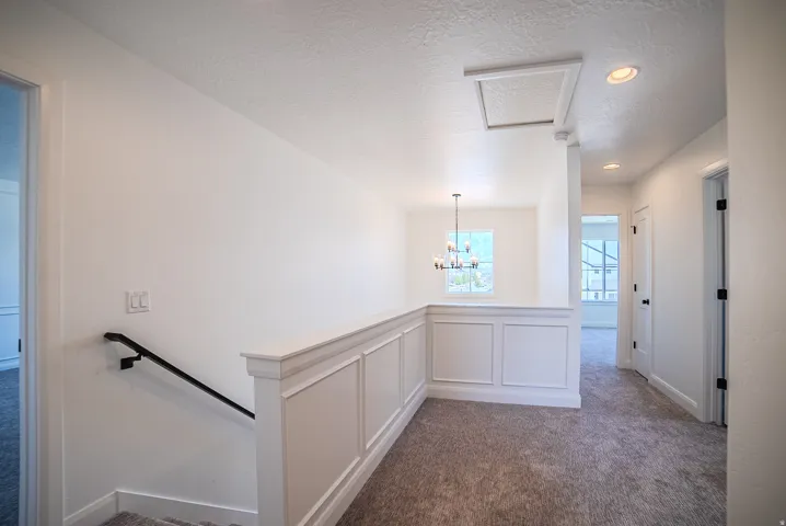 Upper-level landing featuring a white wainscoting half-wall, neutral carpeting, recessed ceiling lighting, and a modern chandelier visible through an opening