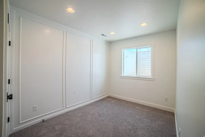Bright interior space featuring recessed lighting, a window, grey carpet flooring, white baseboards, and wainscoting wall accents