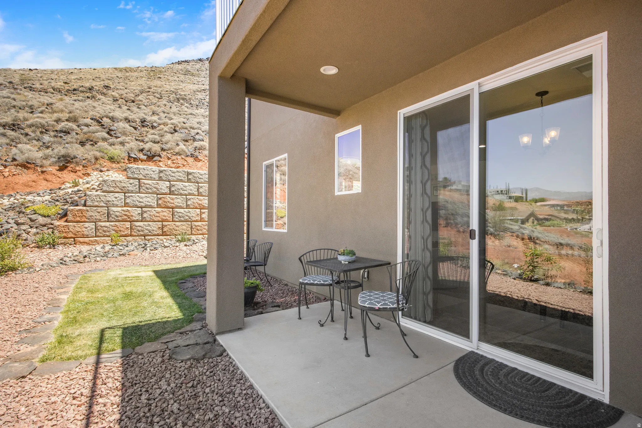 Private covered patio with a concrete slab, framed by a stone retaining wall and natural landscaping