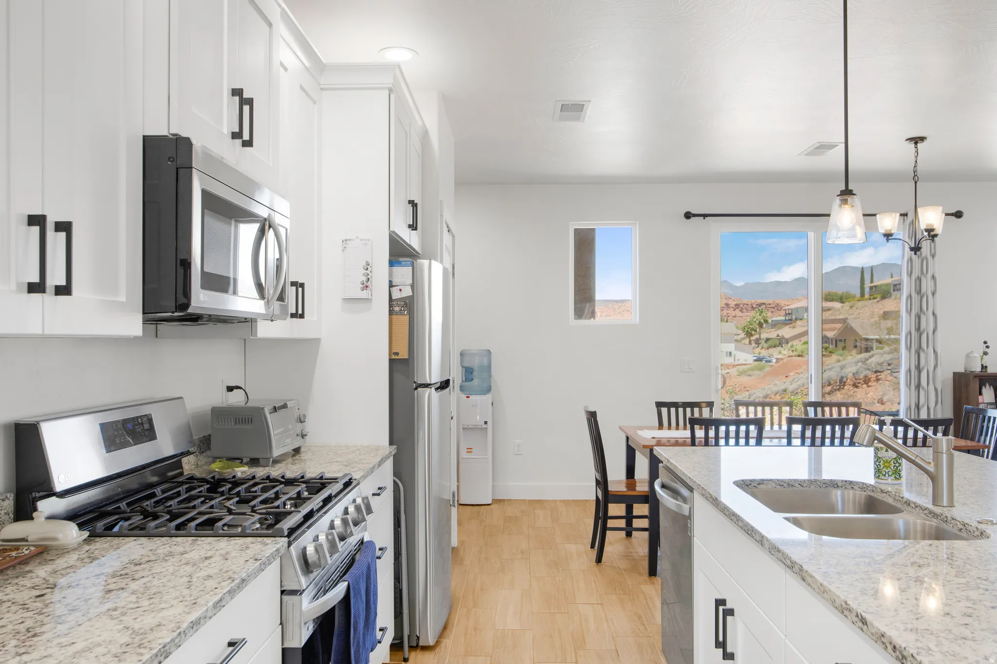 Modern kitchen featuring white shaker cabinetry with black hardware, stainless steel appliances, and light-toned granite countertops