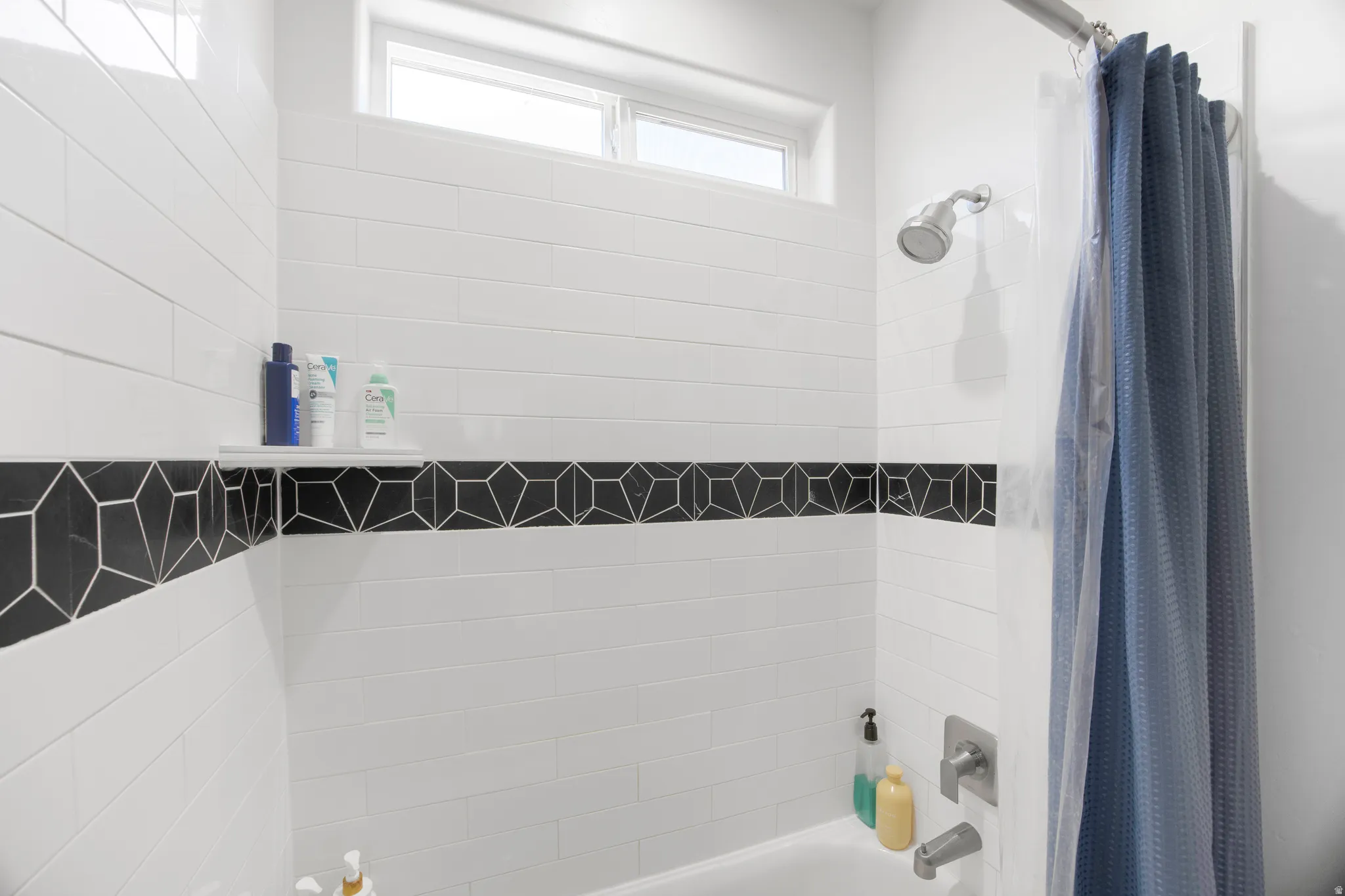 Bathtub-shower combination featuring white subway tile, a decorative black geometric tile accent band, and a brushed nickel shower head and faucet