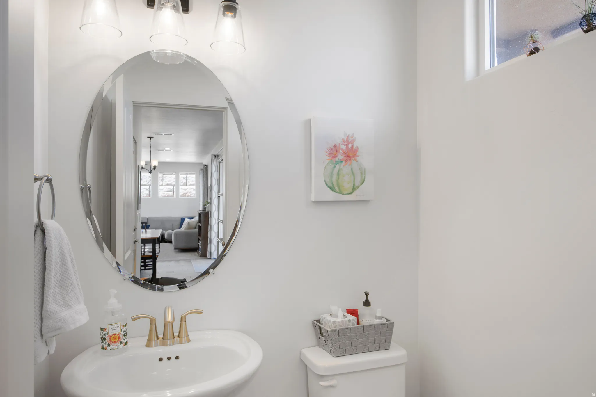 Pedestal sink with brass-finish faucet, an oval mirror, and a three-light vanity fixture