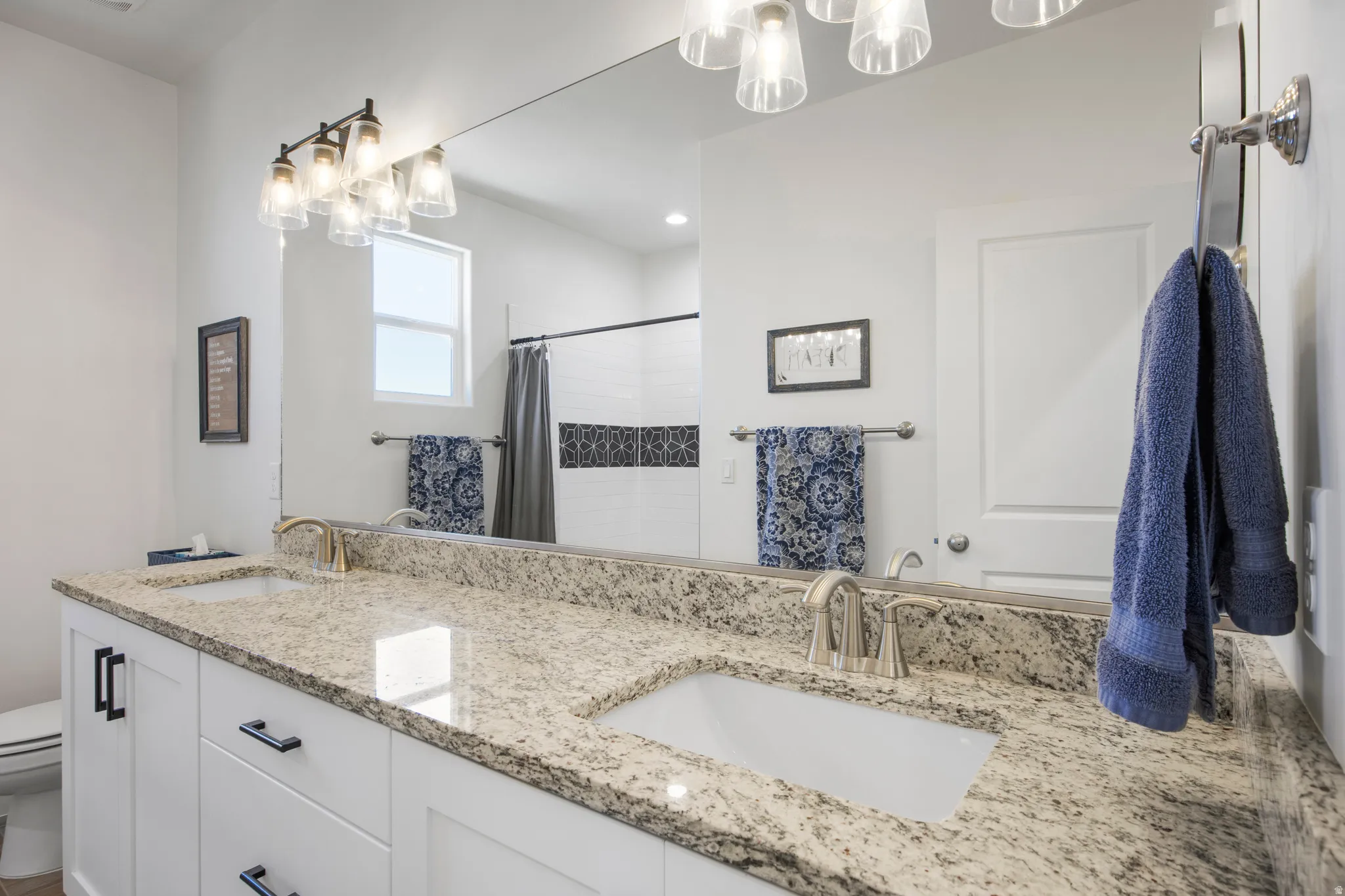Double vanity with integrated sinks, light-toned stone countertop, white cabinetry with black hardware, and an expansive wall-mounted mirror