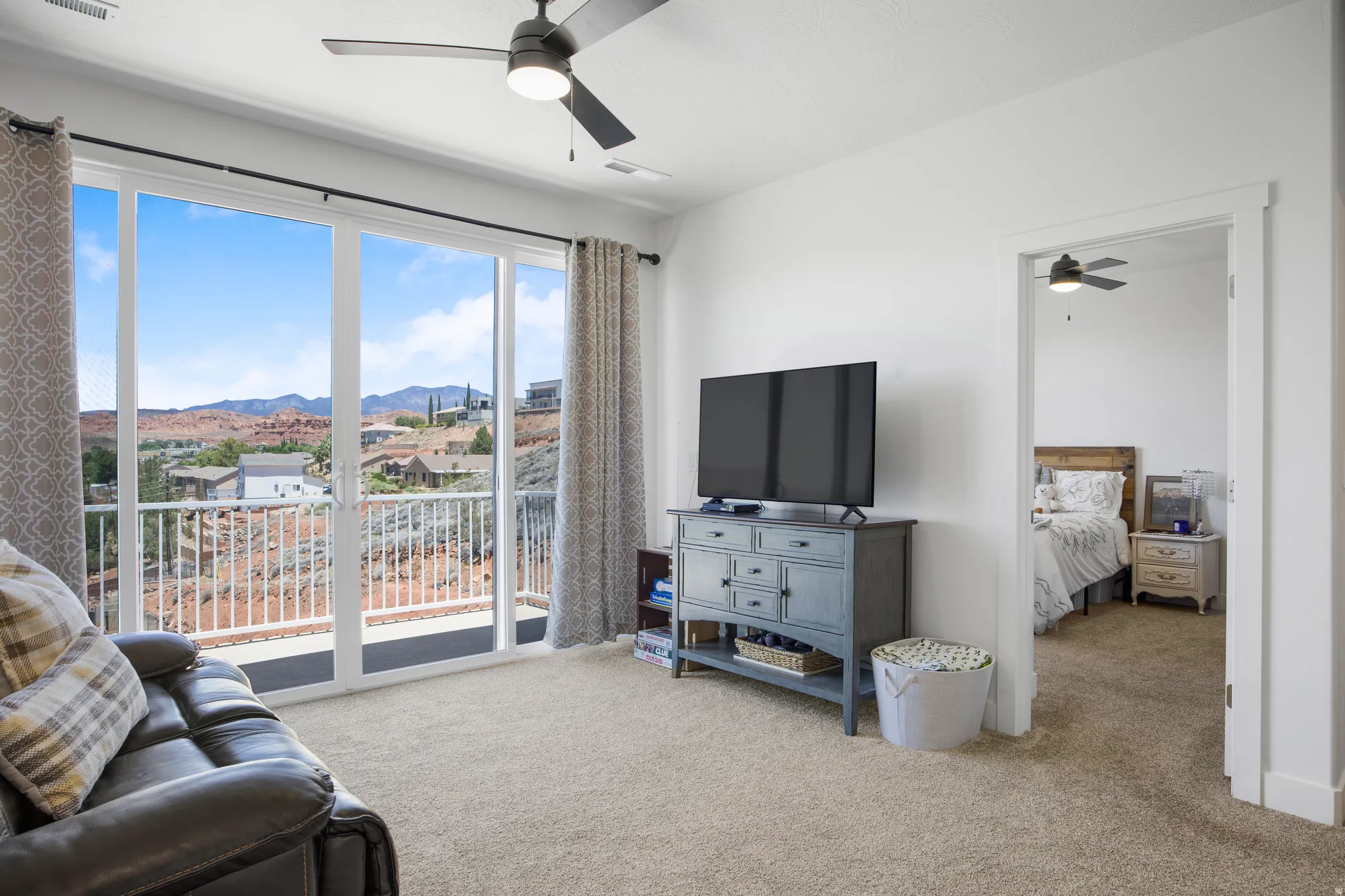 Spacious room with a ceiling fan, light beige carpeting, and a large sliding glass door offering expansive views of the red rock landscape