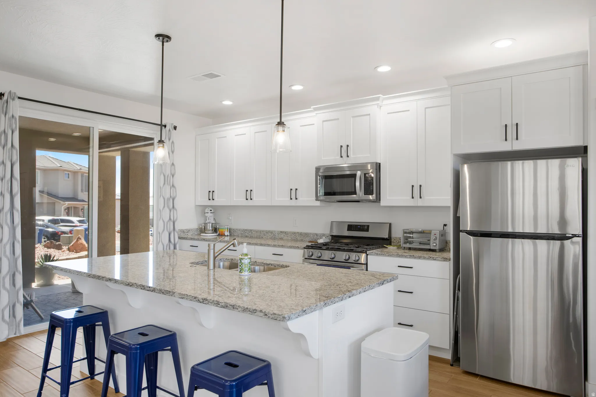 Modern kitchen featuring white cabinetry with dark hardware, stainless steel appliances, and light-toned granite countertops