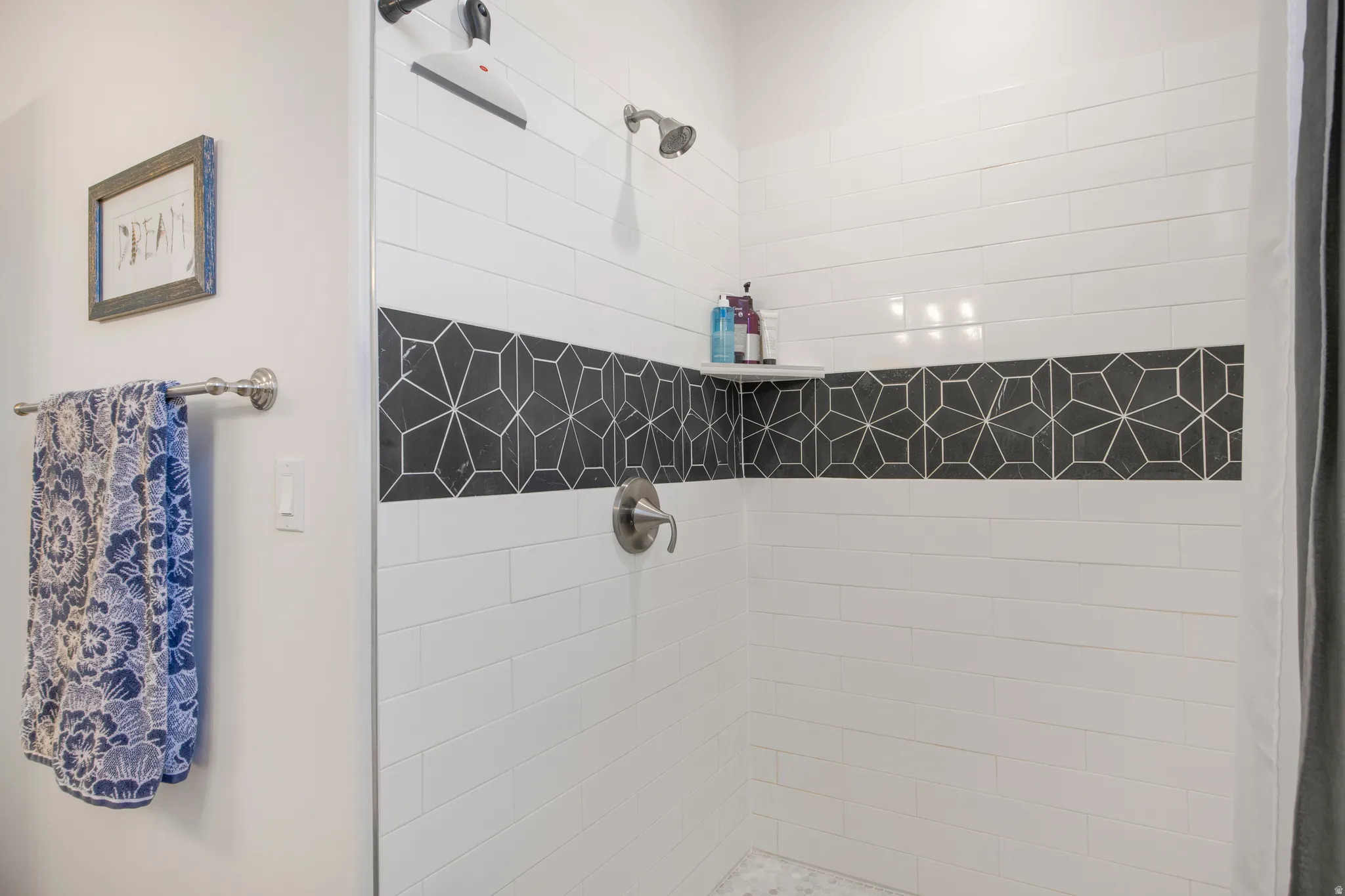 Shower enclosure featuring white subway tile with a geometric pattern accent band