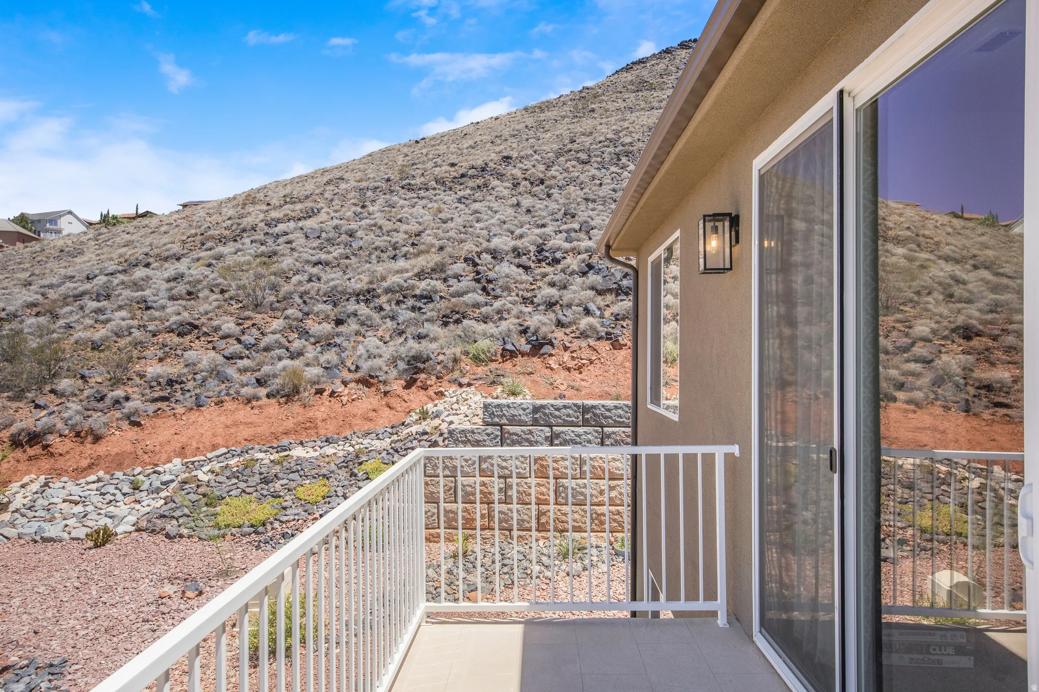 Private balcony featuring a stucco exterior, sliding glass door, white metal railing, and an outdoor wall sconce