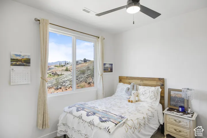 Bedroom featuring a large window, a wood-finish headboard, and a ceiling fan with integrated lighting