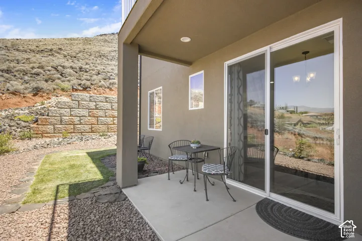 Private covered patio with a concrete slab, framed by a stone retaining wall and natural landscaping