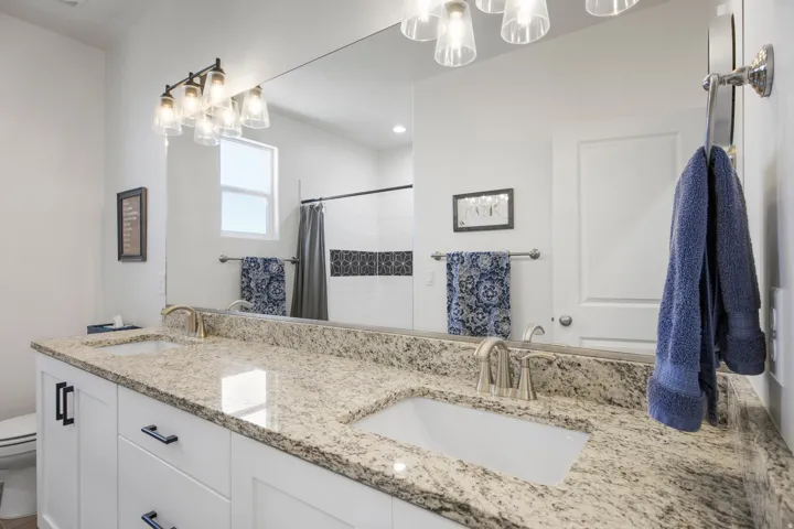 Double vanity with integrated sinks, light-toned stone countertop, white cabinetry with black hardware, and an expansive wall-mounted mirror