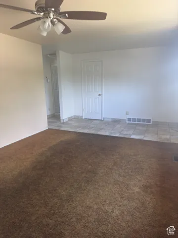 Living area featuring a ceiling fan with integrated lighting, brown carpet flooring, and white painted walls