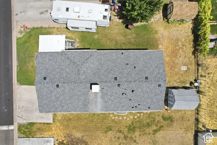 Property featuring a gray asphalt shingle roof, a concrete driveway, a rear yard with a storage shed, and mature trees on the perimeter