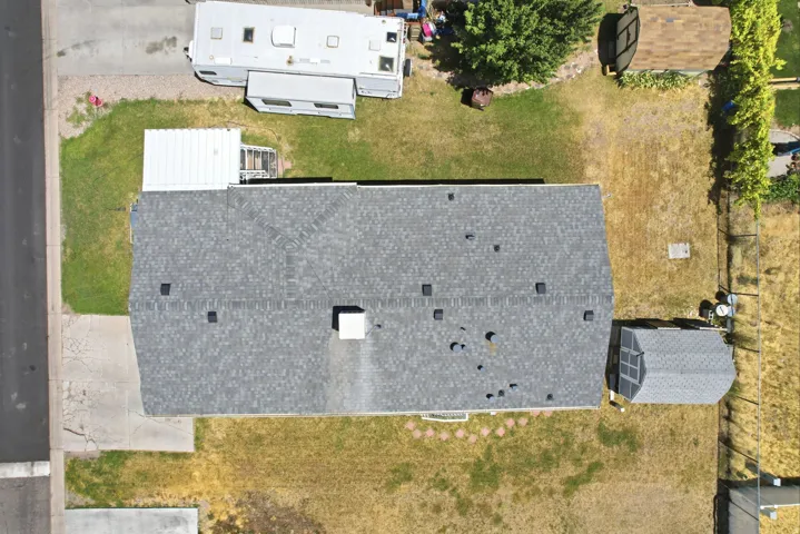 Property featuring a gray asphalt shingle roof, a concrete driveway, a rear yard with a storage shed, and mature trees on the perimeter