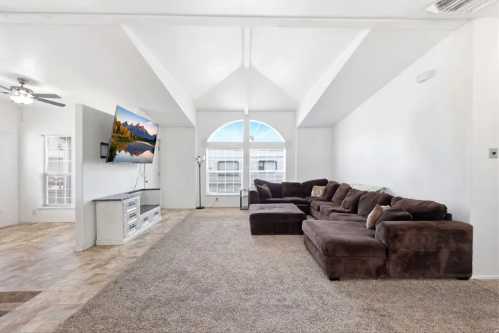 Expansive living area featuring vaulted ceilings with exposed beams, a large arched window, and mixed flooring with carpet and wood-finish planks