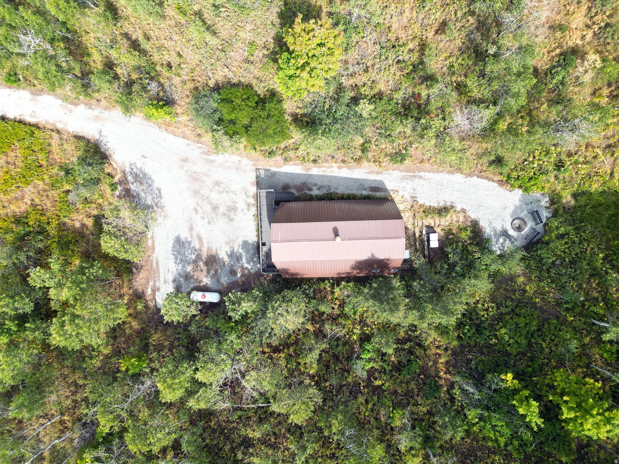 Aerial view showcasing a metal-roofed structure with a gravel driveway, surrounded by green foliage
