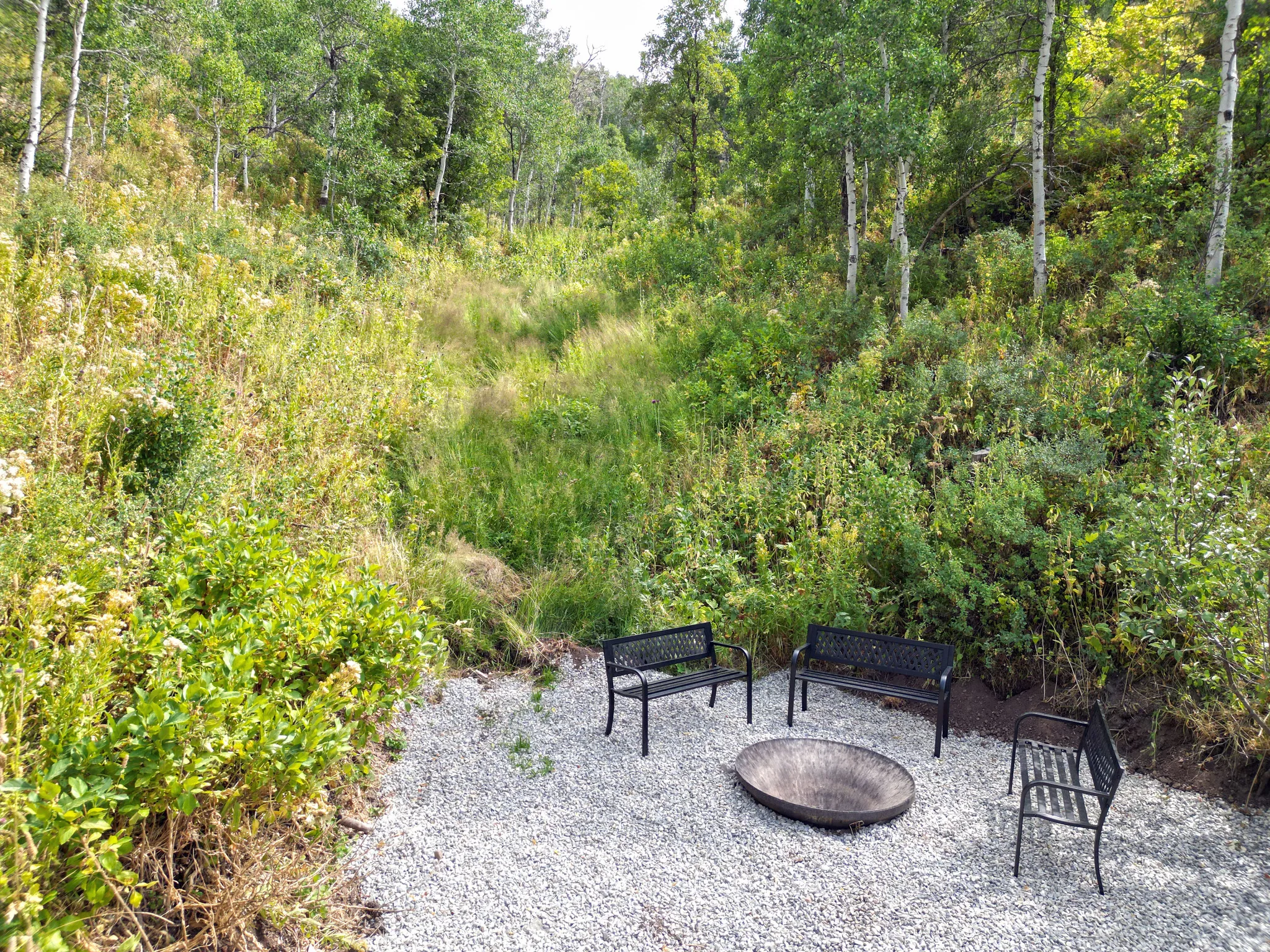 Gravel patio featuring a fire pit with surrounding seating and mature trees