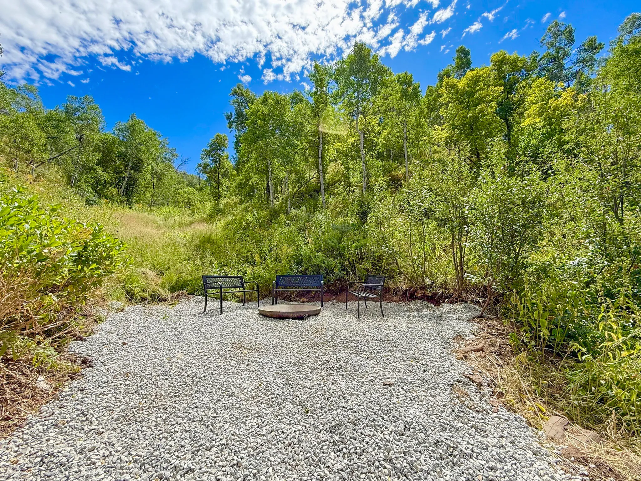 Gravel outdoor area featuring a built-in fire pit surrounded by seating and natural landscaping