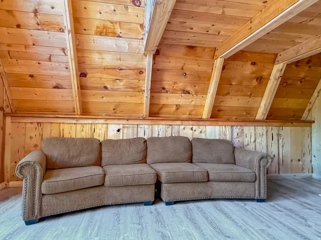 Sloped ceiling with exposed wood beams, natural wood paneling, and wood-finish flooring