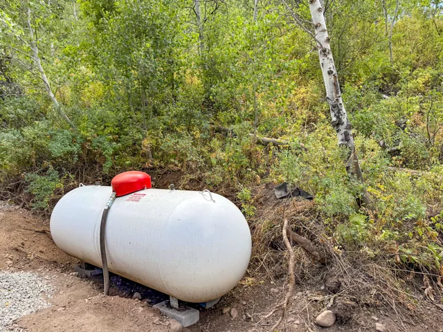 Large white propane tank featuring a red regulator, positioned on concrete blocks, with a hose connection