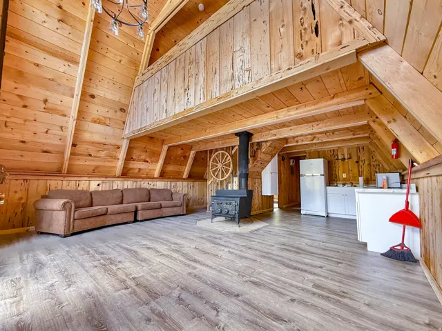 Spacious room with a vaulted wood-paneled ceiling, wood-finish flooring, and a cast iron wood-burning stove