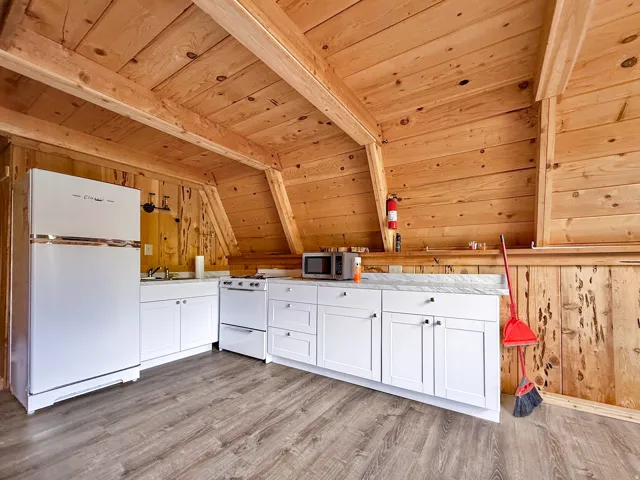 Kitchenette featuring angled wood plank walls and ceiling, white shaker-style cabinetry, a white countertop, and wood-finish flooring