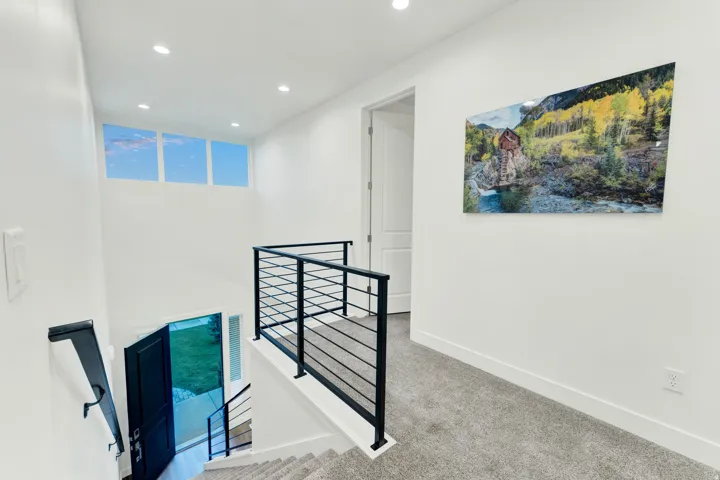 Upper-level landing featuring a modern horizontal bar railing system with a black finish, recessed lighting, and a high transom window