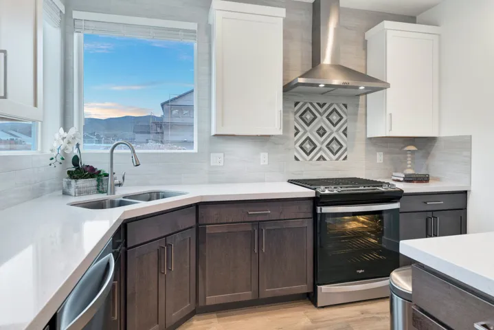 Modern kitchen featuring a dual-tone cabinetry scheme, stainless steel appliances, a geometric tile backsplash accent, light-toned countertops, and a double basin sink